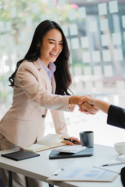 Asyalı kadınlar ve röportajcılar el sıkışıyor. İş adamı, bir ofis konferans odasında iş arkadaşlarıyla masanın etrafında tokalaşırken. karşılama anlaşması konsepti