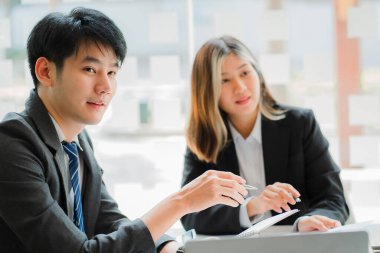 Genç işadamı iş arkadaşlarıyla sohbet ediyor, bilgisayarları paylaşıyor ve mutlu ve kendinden emin bir şekilde gülümsüyor. Finansal belgelerdeki veri analizi ile kavramlar, yüzlerinde bir gülümsemeyle birlikte çalışır..