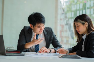 Genç işadamı iş arkadaşlarıyla sohbet ediyor, bilgisayarları paylaşıyor ve mutlu ve kendinden emin bir şekilde gülümsüyor. Finansal belgelerdeki veri analizi ile kavramlar, yüzlerinde bir gülümsemeyle birlikte çalışır..