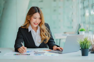 Ofiste çalışan genç Asyalı iş kadını dizüstü bilgisayarında mali grafikle Finansal muhasebe konseptinde çalışıyor.