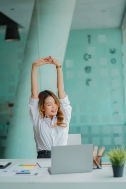 Asian businesswoman relaxing during office work with financial graph on laptop computer desk financial accounting concept