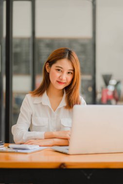 Masasında dizüstü bilgisayarla projesinde çalışan genç ve çekici bir Asyalı iş kadını. dikey resim