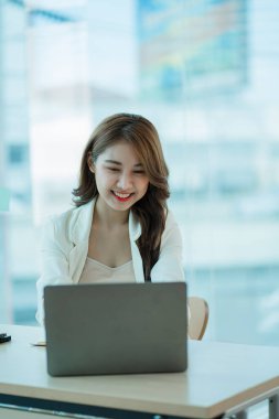 Masasında dizüstü bilgisayarla projesinde çalışan genç ve çekici bir Asyalı iş kadını. dikey resim