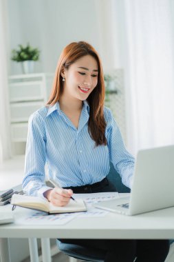 Masasında dizüstü bilgisayarla projesinde çalışan genç ve çekici bir Asyalı iş kadını. dikey resim