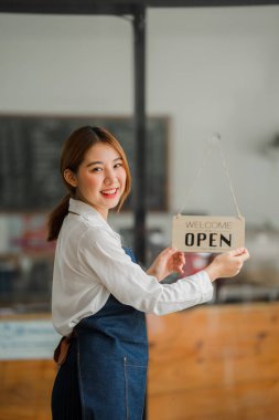 Kafe kapısının önünde açık bir tabelayla önlüklü güzel bir Asyalı barista. işletme sahibi başlangıç fikirleri
