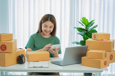 Küçük işletme girişimi, KME, Asyalı kadın girişimcilerin sahibi çevrimiçi satışlar için bir kutu fikir hazırlamak amacıyla online satın alma siparişlerini almak ve kontrol etmek için bir dizüstü bilgisayar kullanın.