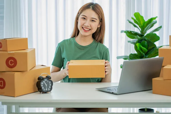 Small business start-up, SME, owner of Asian female entrepreneurs Use a laptop computer to pick up and check online purchase orders to prepare a box of ideas for online sales.