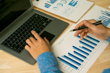 Elinde kalem ve kağıt tutmakta olan işadamı, ofis kavramı muhasebesinde dizüstü bilgisayar kullanarak yıllık iş raporunu hesaplıyor.