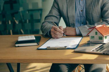 Emlakçı ev kiralama ve satın alma konusunda fikir üretiyor, çalışan satış sözleşmesi teklif ediyor ve ev modeli de masada..