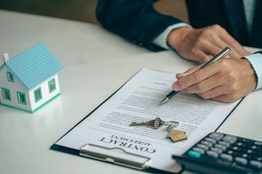 Real estate agent ideas about renting and buying a house, the employee is offering a contract of sale and with the house model on the table.
