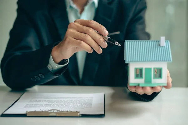 Real estate agent ideas about renting and buying a house, the employee is offering a contract of sale and with the house model on the table.