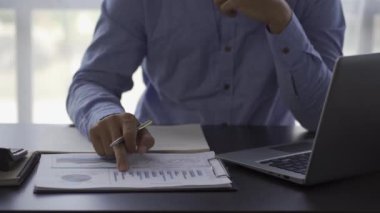a business man looking at a financial chart on a notebook cheerful man analyzingwork in the office Gadgets and documents with graphs and data. 4k video.