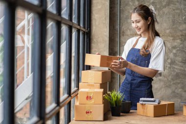 Küçük işletme kuruluşu KME, Asyalı bir bayan girişimcinin sahibi, paketleme kutularını hazırlamak için online siparişleri almak ve kontrol etmek için bir dizüstü bilgisayar kullanıyor. İnternette fikirler satmak, kargo paketleri.