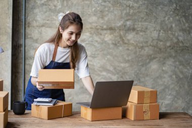 Küçük işletme kuruluşu KME, Asyalı bir bayan girişimcinin sahibi, paketleme kutularını hazırlamak için online siparişleri almak ve kontrol etmek için bir dizüstü bilgisayar kullanıyor. İnternette fikirler satmak, kargo paketleri.