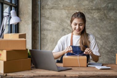 Küçük işletme kuruluşu KME, Asyalı bir bayan girişimcinin sahibi, paketleme kutularını hazırlamak için online siparişleri almak ve kontrol etmek için bir dizüstü bilgisayar kullanıyor. İnternette fikirler satmak, kargo paketleri.
