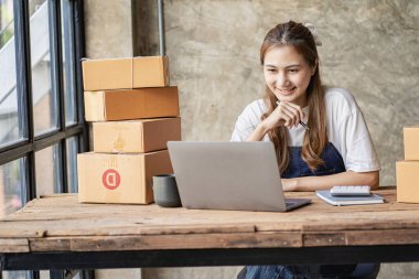 Küçük işletme kuruluşu KME, Asyalı bir bayan girişimcinin sahibi, paketleme kutularını hazırlamak için online siparişleri almak ve kontrol etmek için bir dizüstü bilgisayar kullanıyor. İnternette fikirler satmak, kargo paketleri.