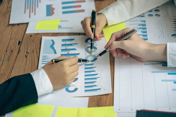 A diverse group of international executive business partners discuss reports at the board of directors\' table. The team is negotiating a project, developing a business strategy, analyzing, calculating, graphing documents with a laptop in the office.