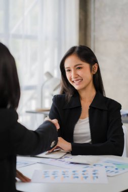 İki gülümseyen bayan iş ortağı ofis ofis ofis çalışanı kızla el sıkışıyor ve mali grafik ve dizüstü bilgisayarı tartışmak için bir anlaşma yapıyor.