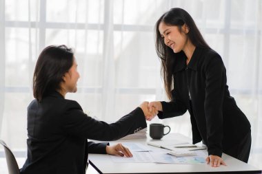 İki gülümseyen bayan iş ortağı ofis ofis ofis çalışanı kızla el sıkışıyor ve mali grafik ve dizüstü bilgisayarı tartışmak için bir anlaşma yapıyor.