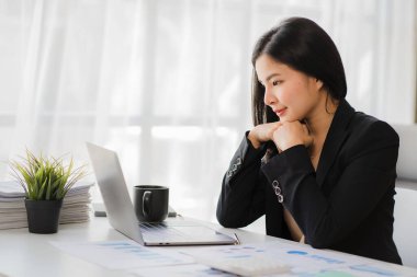 Happy Asian businesswoman using laptop computer while doing financial work. Successful with financial documents on the table