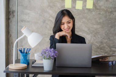 Happy Asian businesswoman using laptop computer while doing financial work. Successful with financial documents on the table