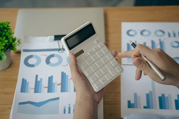 A businessman presses a white calculator to calculate numbers in company financial documents. The finance department prepares accounting documents, analyzing income and expenses in the business.