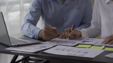 Business team statistical analysis of business data in a meeting graph on a laptop that analyzes the data. Two coworkers are overworked as they brainstorm documents and graphs to present solutions. 4k video