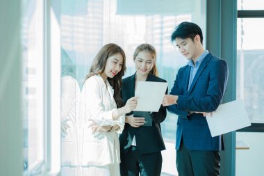 Genç Asyalı iş adamları finansal belgelerde dizüstü bilgisayarlarla mutlu bir şekilde çalışıyorlar. Bir grup iş adamı modern bir ofis tasarım ve konsept planlamada toplanıyor.