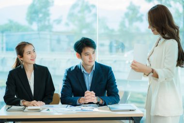 Genç Asyalı iş adamları finansal belgelerde dizüstü bilgisayarlarla mutlu bir şekilde çalışıyorlar. Bir grup iş adamı modern bir ofis tasarım ve konsept planlamada toplanıyor.