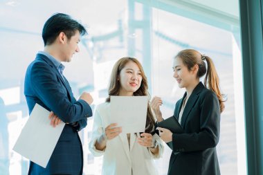 Genç Asyalı iş adamları finansal belgelerde dizüstü bilgisayarlarla mutlu bir şekilde çalışıyorlar. Bir grup iş adamı modern bir ofis tasarım ve konsept planlamada toplanıyor.