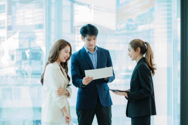 Genç Asyalı iş adamları finansal belgelerde dizüstü bilgisayarlarla mutlu bir şekilde çalışıyorlar. Bir grup iş adamı modern bir ofis tasarım ve konsept planlamada toplanıyor.