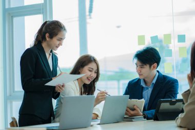 Genç Asyalı iş adamları finansal belgelerde dizüstü bilgisayarlarla mutlu bir şekilde çalışıyorlar. Bir grup iş adamı modern bir ofis tasarım ve konsept planlamada toplanıyor.