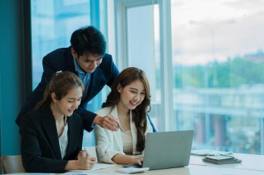 Genç Asyalı iş adamları finansal belgelerde dizüstü bilgisayarlarla mutlu bir şekilde çalışıyorlar. Bir grup iş adamı modern bir ofis tasarım ve konsept planlamada toplanıyor.