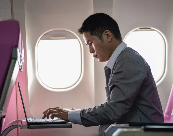 Asian man sitting comfortably in business class Businessman working on a laptop computer and smartphone during an airplane flight