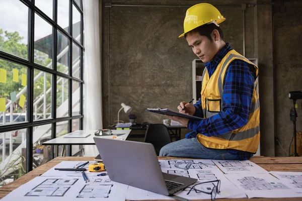 Young Asian architect working on blueprints in the office. A young engineer works using a laptop computer at a building site office.