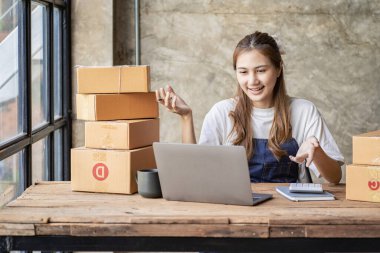 Küçük bir işletmenin portresi, KME sahibi, genç Asyalı girişimci, çalışıyor, kutuları açıyor, siparişleri kontrol ediyor. KME müşterilerine satılmak üzere paket teslimat kutularını çevrimiçi iş fikirlerine hazırlamak için