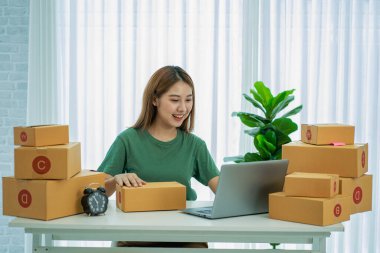Küçük bir işletmenin portresi, KME sahibi, genç Asyalı girişimci, çalışıyor, kutuları açıyor, siparişleri kontrol ediyor. KME müşterilerine satılmak üzere paket teslimat kutularını çevrimiçi iş fikirlerine hazırlamak için