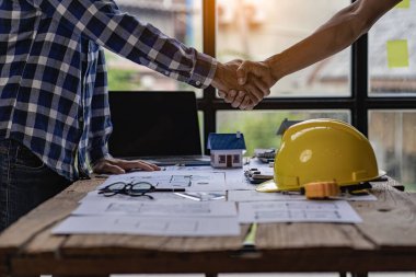Architect engineers shake hands with hats and houses on construction tool tables. with blueprints on the table - business teamwork working together Successful Collaboration Ideas
