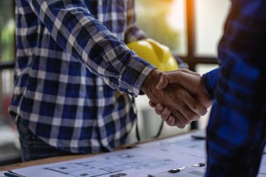 Architect engineers shake hands with hats and houses on construction tool tables. with blueprints on the table - business teamwork working together Successful Collaboration Ideas