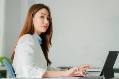 Beautiful smiling Asian businesswoman working using a tablet at the office while sitting in a modern office successful business idea