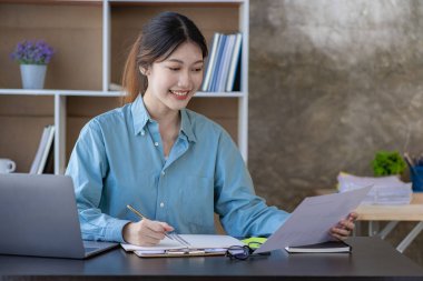A young Asian female accountant or manager sits at her desk. Reading and reviewing account sales in reports