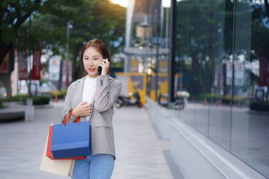 Smiling Asian woman with colored shopping bags on shopping mall background and looking happy Smiling shopping while standing in front of a department store lifestyle concept