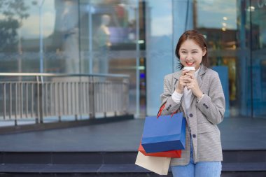 Smiling Asian woman with colored shopping bags on shopping mall background and looking happy Smiling shopping while standing in front of a department store lifestyle concept