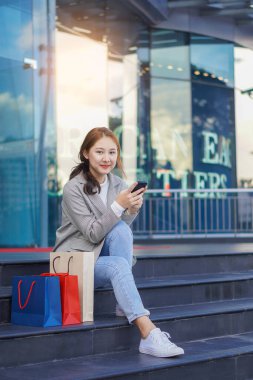 Smiling Asian woman with colored shopping bags on shopping mall background and looking happy Smiling shopping while standing in front of a department store lifestyle concept