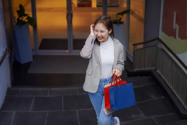 Smiling Asian woman with colored shopping bags on shopping mall background and looking happy Smiling shopping while standing in front of a department store lifestyle concept
