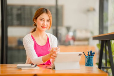 Happy Asian female student wearing headphones, studying online, watching webinars, podcasts on tablets, listening, learning, education courses. online meeting