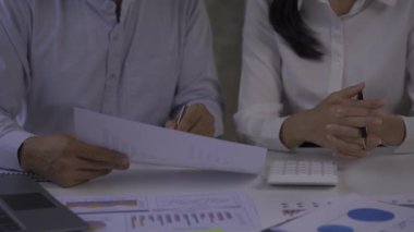 Two young businessmen in a graph pointing to a meeting in a laptop analyzing data. Old man CEO talking to customers in office 4k