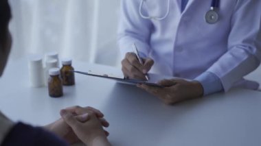 Close-up view Male doctor, unknown name, therapist, male doctor in white dress, sitting at the table, consulting the patient, complaining, giving medical advice, explaining, treatment table, prescription, 4k
