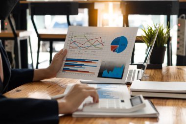 Businesswoman holding documents with financial statistics, stock photos, discussion and data analysis, charts and graphs with laptop computer. financial concept