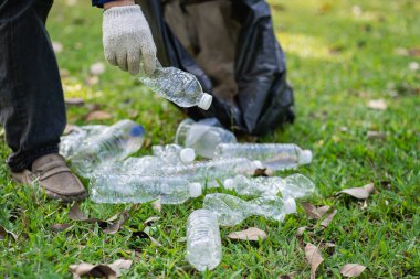 Hand picks up plastic bottles up close with young man volunteering to collect plastic bottles in garbage bags for environmental protection in the ecological forest background. recycling concept